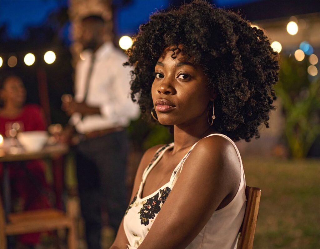 a photo of a black woman sitting alone, looking just slightly anxious at a evening party